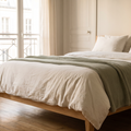 Chambre slow living à la lumière du soir, lit en percale lavée blanc cassé et plaid en maille vert sauge