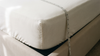 Angle de matelas épais avec un drap-housse en coton blanc et un mètre ruban mesurant la hauteur de bonnet
