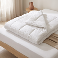 Couette blanche repliée sur un lit, montrant son gonflant, dans une chambre à la lumière douce