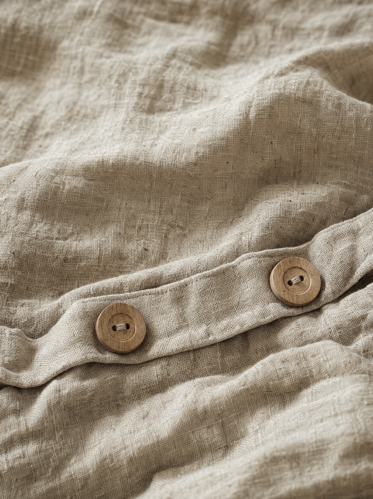 Gros plan sur le tissage irrégulier du lin lavé Noctua Paris et les boutons en bois naturel