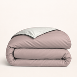 Housse de couette en coton égyptien rose champagne — housse seule pliée, revers champagne, fond ivoire — Noctua Paris.