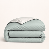 Housse de couette en coton égyptien vert sauge — housse seule pliée, revers crème clair, fond ivoire — Noctua Paris.
