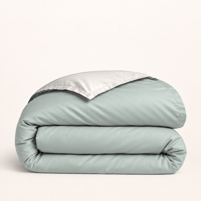 Housse de couette en coton égyptien vert sauge — housse seule pliée, revers crème clair, fond ivoire — Noctua Paris.