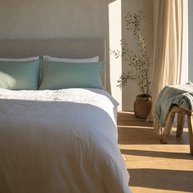 Taies d'oreiller coton doux vert d'eau Noctua Paris sur un lit, soleil rasant sur le parquet