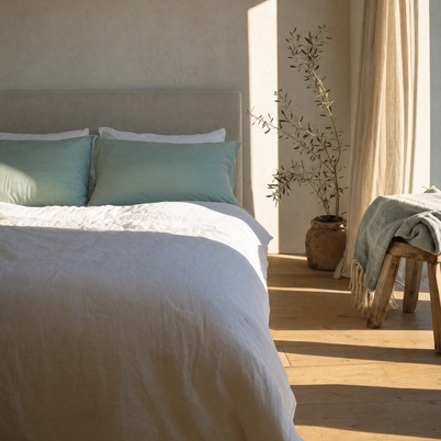 Taies d'oreiller coton doux vert d'eau Noctua Paris sur un lit, soleil rasant sur le parquet