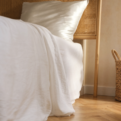 Taie d'oreiller en soie de mûrier blanche Noctua Paris sur un lit à tête de lit en rotin, lumière du matin