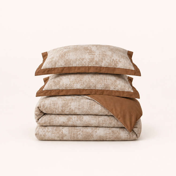 Noctua Paris — Parure de lit en gaze de coton caramel, deux taies à bordure unie et housse pliée, sur fond ivoire.