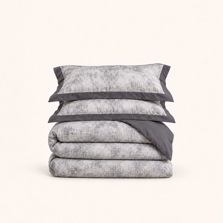 Noctua Paris — Parure de lit en gaze de coton gris, deux taies à bordure unie et housse pliée, sur fond ivoire.