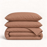 Parure de lit en percale de coton terracotta — deux taies et une housse pliée sur fond ivoire — Noctua Paris